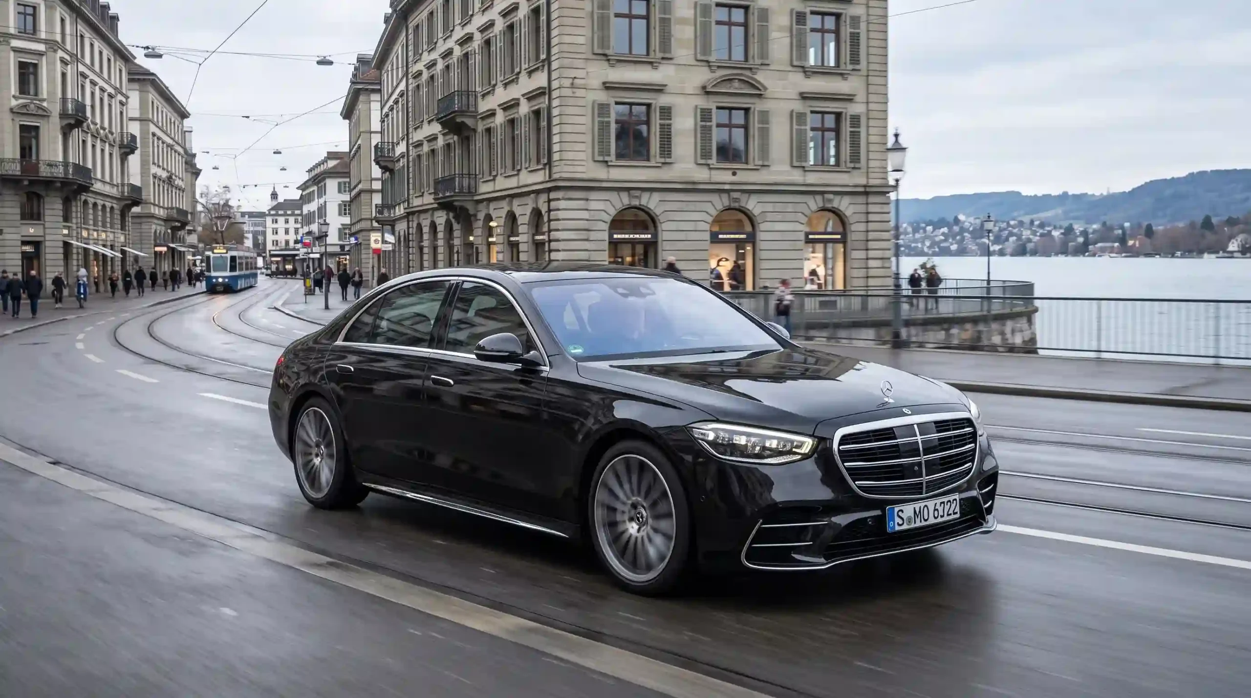 Black Mercedes-Benz sedan driving along a Swiss city street beside a lake