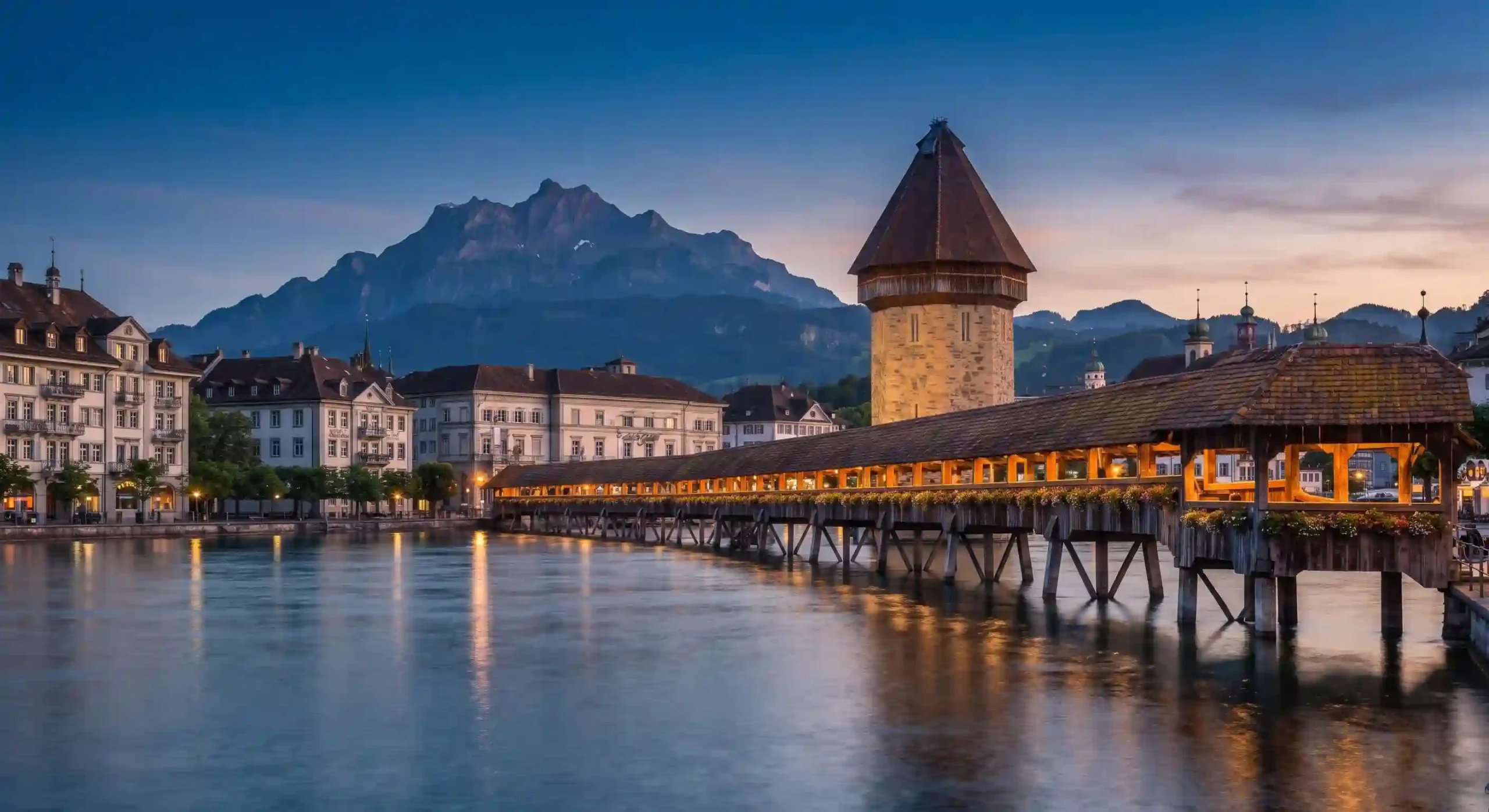 Historic wooden Chapel Bridge (Kapellbrücke) and water tower in Lucerne with Lake Lucerne and snowy mountains in the background